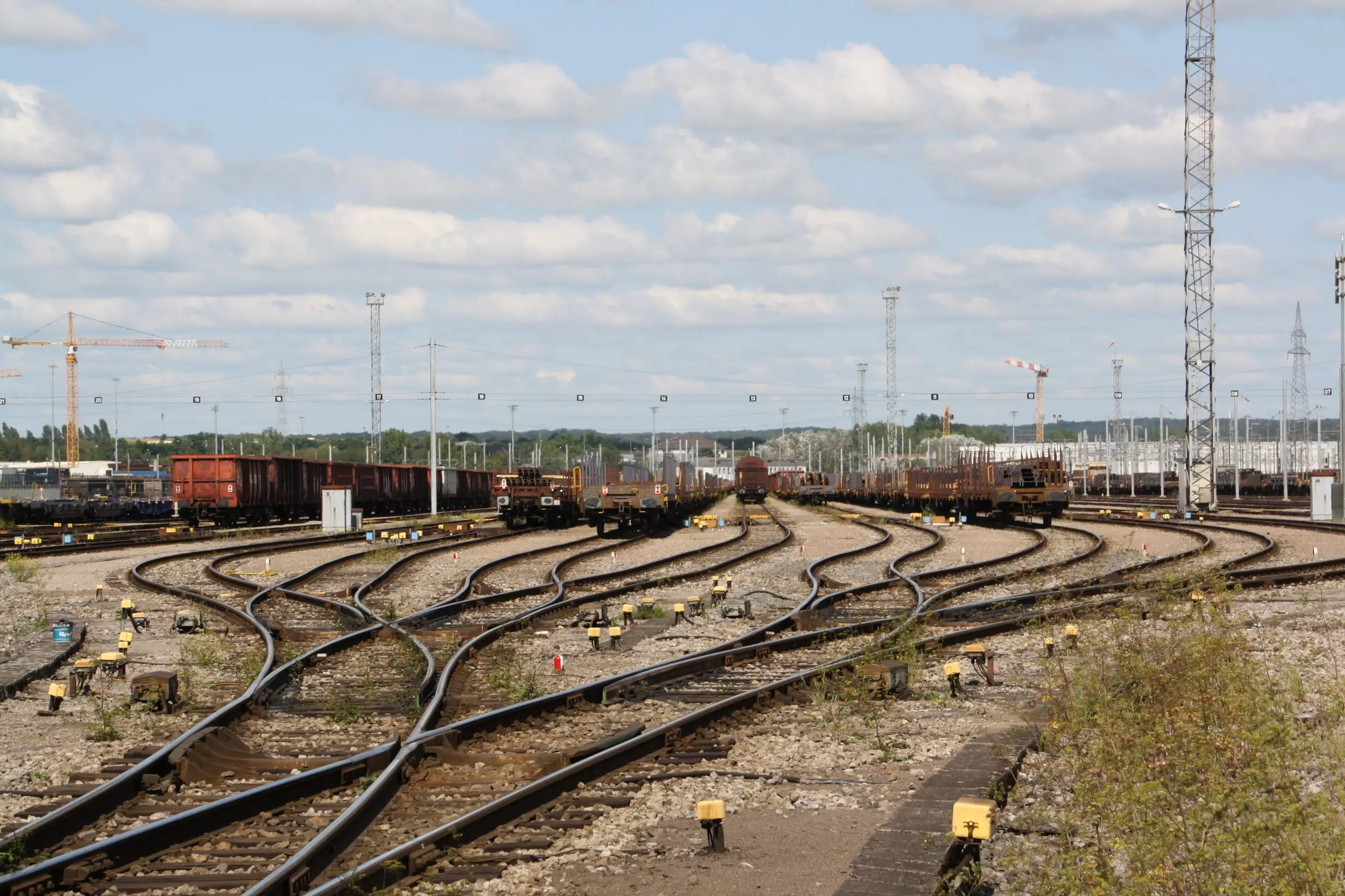 Großer Rangierbahnhof mit Güterwaggons, Signalanlagen und Industriegebäuden im Hintergrund.